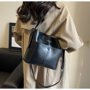 Model showing a black PU leather bucket bag with a front pocket and gold text detail