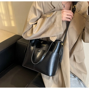 Detail view of black leather bucket bag with top handle and gold logo on a model