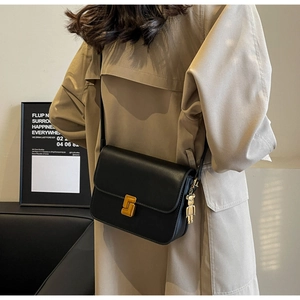 Close-up of black leather crossbody bag featuring gold buckle and bear charm detail