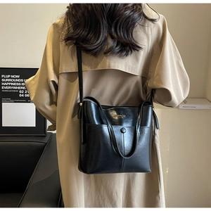 Detail of black faux leather bucket bag featuring gold Fashion Bag logo and front snap pocket