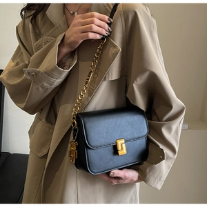 Close-up of black crossbody square bag with gold lock, chain strap, and bear charm