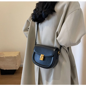 Borsa a sella in pelle nera su modella con trench beige e fibbia in metallo dorato