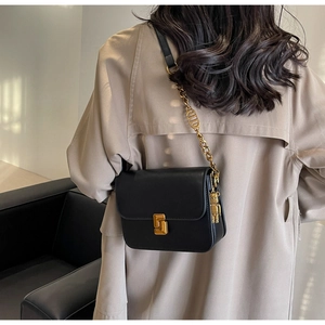 Detail of black matte leather shoulder bag with gold chain and bear charm accent