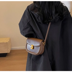 Dettaglio di una borsa a sella marrone con chiusura quadrata dorata sulla modella