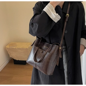 Detail of dark brown leather bucket bag shown on a model wearing a long black coat