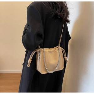 Detail of khaki pleated bucket bag with silver chain worn over a black blazer