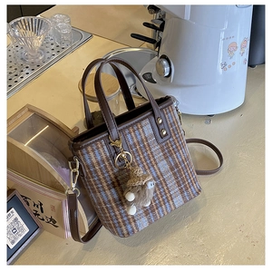Detail of vintage plaid bucket bag with plush charm on a coffee shop bar counter