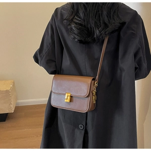 Macro detail of dark brown leather crossbody bag with gold bear charm and clasp
