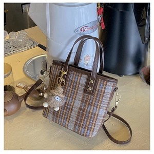 Detail of wool plaid tote bag with brown leather straps and plush bear charm