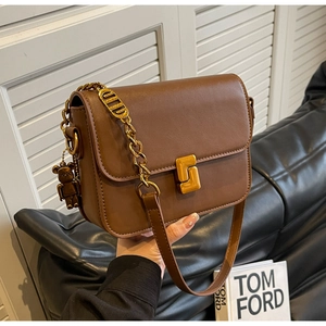 Close-up of brown crossbody bag featuring golden buckle, chain strap and bear charm
