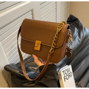 Detail of a brown leather crossbody bag with golden S-clasp and bear charm accessory