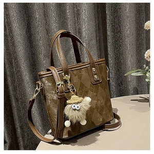 Detail of brown quilted bucket bag with plush monster charm and gold metal accents