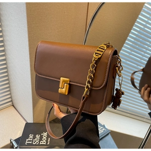Detail of a brown leather crossbody bag with gold twist lock and a cute bear charm