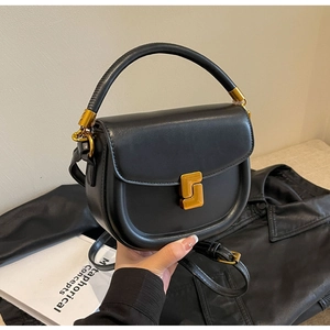 Dettaglio di una borsa a sella in pelle nera con fibbia dorata e manico superiore