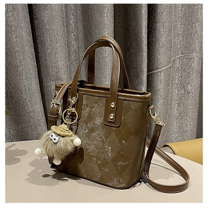 Close-up of brown quilted leather bucket bag with vintage finish and plush monster charm