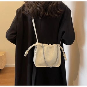 Detail of off-white drawstring bucket bag with silver chain on black blazer outfit