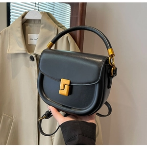 Dettaglio borsa a sella in pelle nera con fibbia dorata geometrica e manico superiore