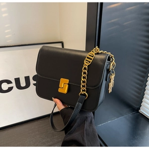 Detail of black crossbody bag with golden S-clasp and bear charm accessory