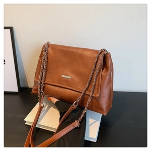 Detail of dark brown leather tote bag showing silver metal plate and chain strap