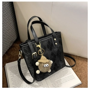 Detail of black diamond-quilted bucket bag with plush monster charm and leather strap