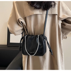 Detail of black bucket bag with silver chain strap and drawstring closure on a model