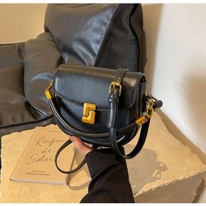 Dettaglio borsa a sella in pelle nera con fibbia dorata geometrica e finitura liscia