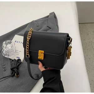 Detail of black leather crossbody bag featuring gold metal clasp and iconic bear pendant