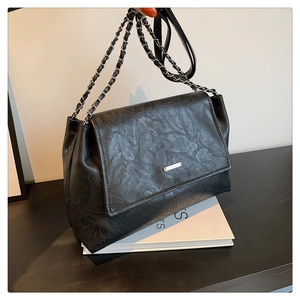 Detail of black textured leather tote bag with silver chain strap on white book background