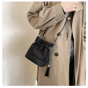 Detail of black glitter bucket bag with chain strap and tassel on beige coat
