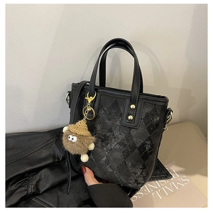 Detail of black quilted leather bucket bag with plush monster charm and metal hardware