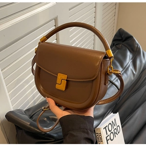 Dettaglio di una borsa a sella in pelle marrone scuro con fibbia dorata e manico