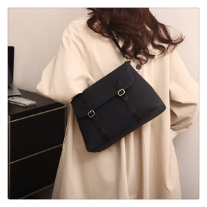 Close-up of matte black tote bag with gold metal buckles shown on a beige trench coat