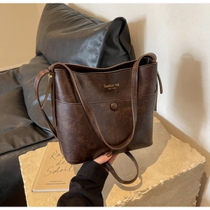 Close-up of a vintage dark brown bucket bag with gold lettering on a white stone base