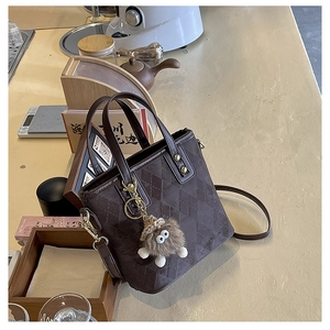 Detail view of a vintage dark brown quilted bucket bag with a plush doll charm on a counter