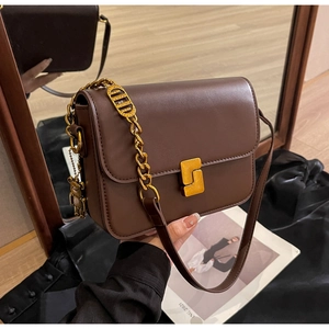 Close-up of brown leather bag with golden chain, square lock, and cute bear pendant