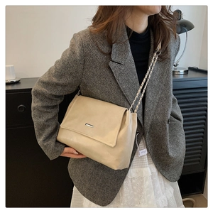Detail of beige leather tote bag featuring a silver metal bar and woven chain strap