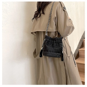Detail of black sequined bucket bag with chain strap and fringe on trench coat