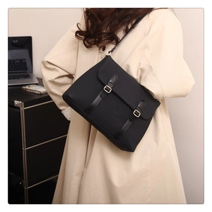 Detail of a black crossbody messenger bag with leather straps and gold metal buckles
