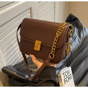 Detail of dark brown leather crossbody bag with gold buckle and bear charm