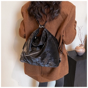 Detail of a large black crinkled leather tote backpack worn by a model in a minimal setting