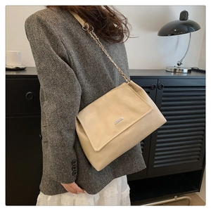 Detail of a beige leather shoulder bag featuring a metal clasp and chain strap on a model