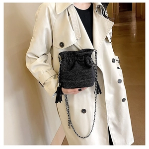 Detail of black glitter bucket bag with drawstring, tassel, and woven chain strap