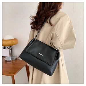 Detail of black faux leather tote with silver metal buckle and chain strap on shoulder
