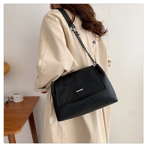 Detail of black faux leather tote with silver metal bar buckle and woven chain strap