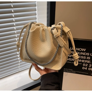 Detail of beige bucket bag featuring litchi grain texture and silver chain strap