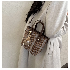 Detail of plaid bucket bag featuring leather handles and a plush monster charm on an autumn coat