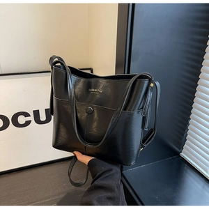Close-up of black bucket bag with gold lettering and polished synthetic leather texture