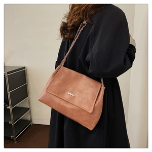 Detail of a brown leather crossbody bag with metal chain strap and minimalist metal bar