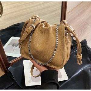 Detail of khaki bucket bag with pleated texture, silver chain, and leather strap