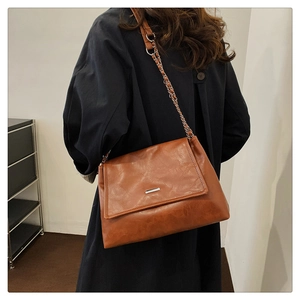 Detail of vintage brown tote bag with metal chain strap and decorative silver plaque